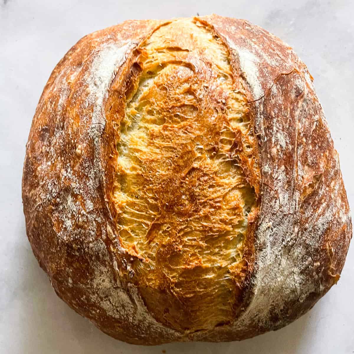 A loaf of no knead whole wheat bread on a white counter.
