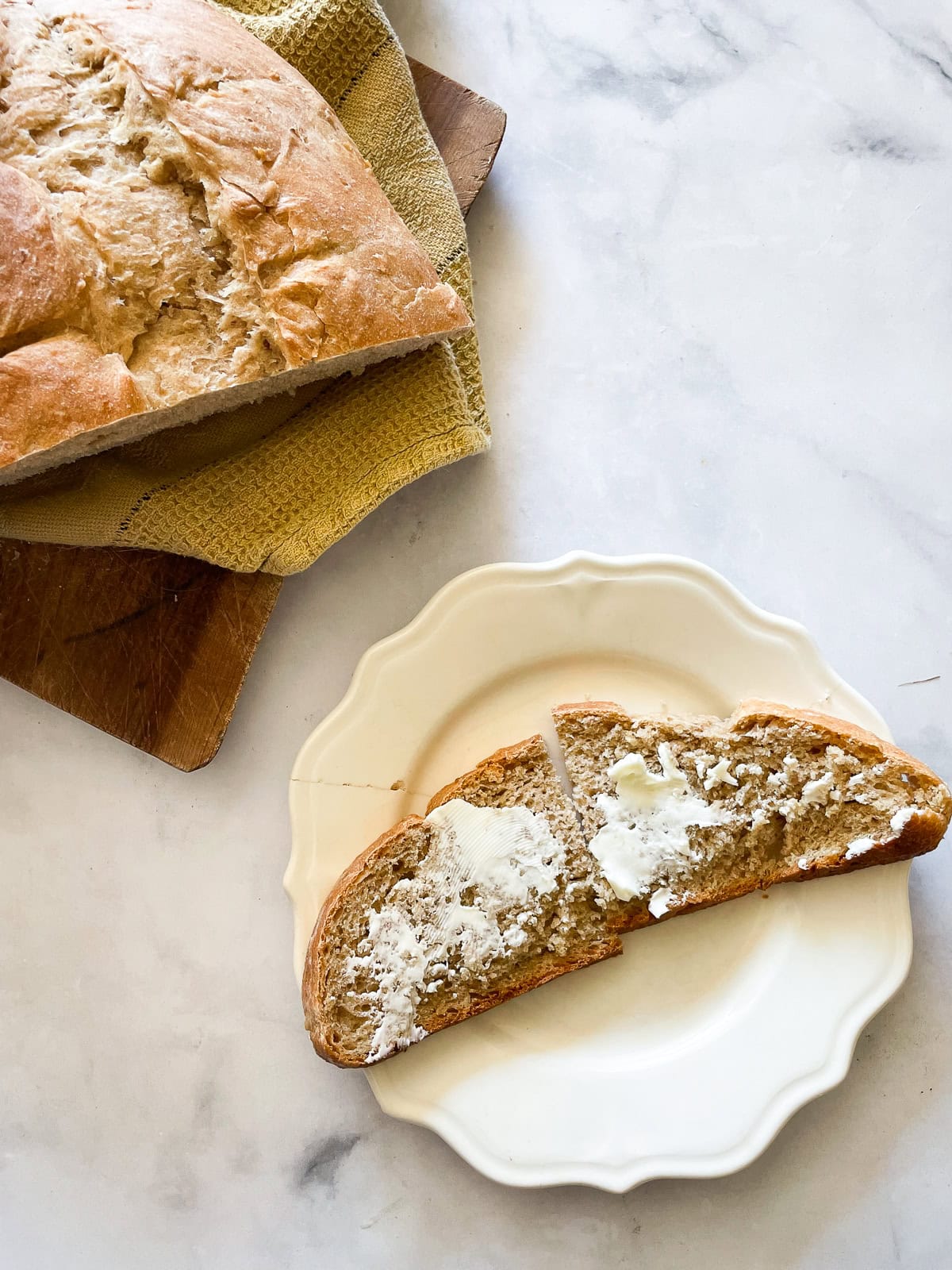 This porridge bread recipe turns leftover oatmeal into a beautifully soft and wholesome loaf! A great way to make sure nothing goes to waste. A slice of porridge bread with butter on a plate with the loaf next to it.
