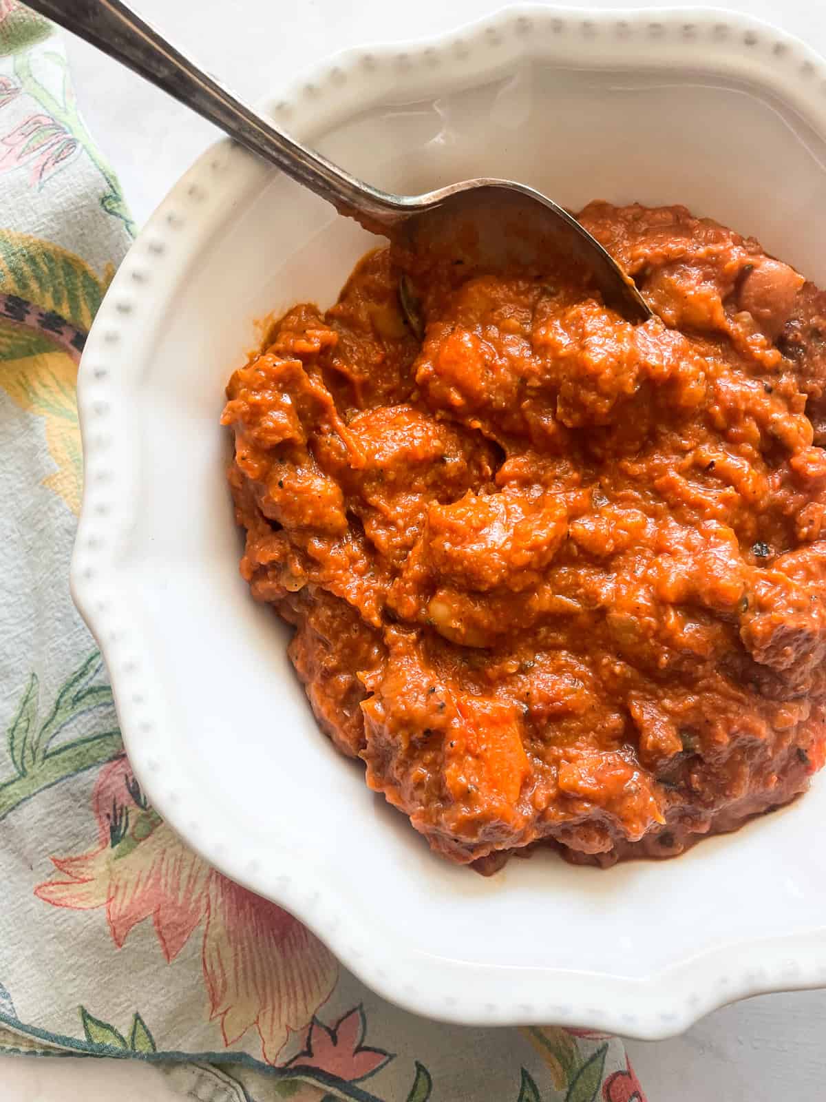 Dig into a hearty bowl of vegetarian white chili that features tender white beans swirled in a rich tomatoey base. A spoon stirs a bowl of vegetarian white chili.