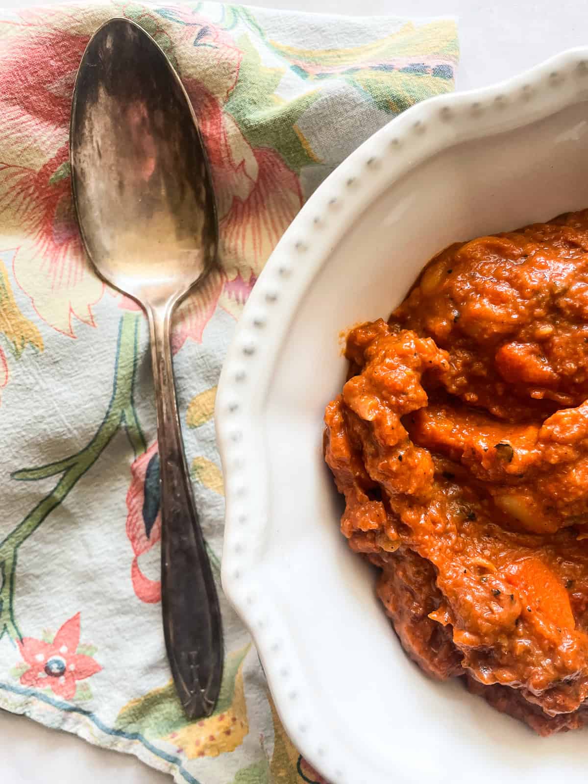 Dig into a hearty bowl of vegetarian white chili that features tender white beans swirled in a rich tomatoey base. A bowl of vegetarian white chili with a spoon next to it.
