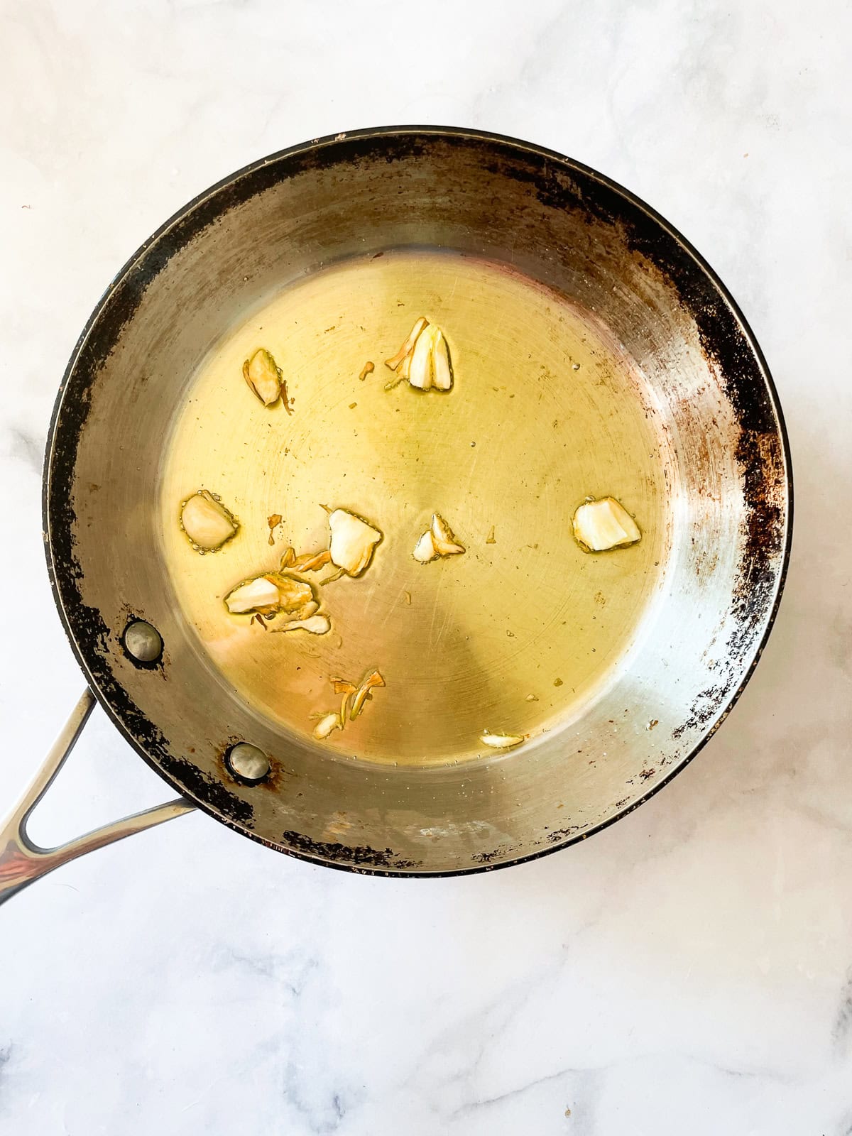 This easy, vegetarian kale pasta sauce is made from garlic sizzled in olive oil, bright green kale, and a bit of lemon zest for extra flavor. Garlic simmers in olive oil in a skillet.