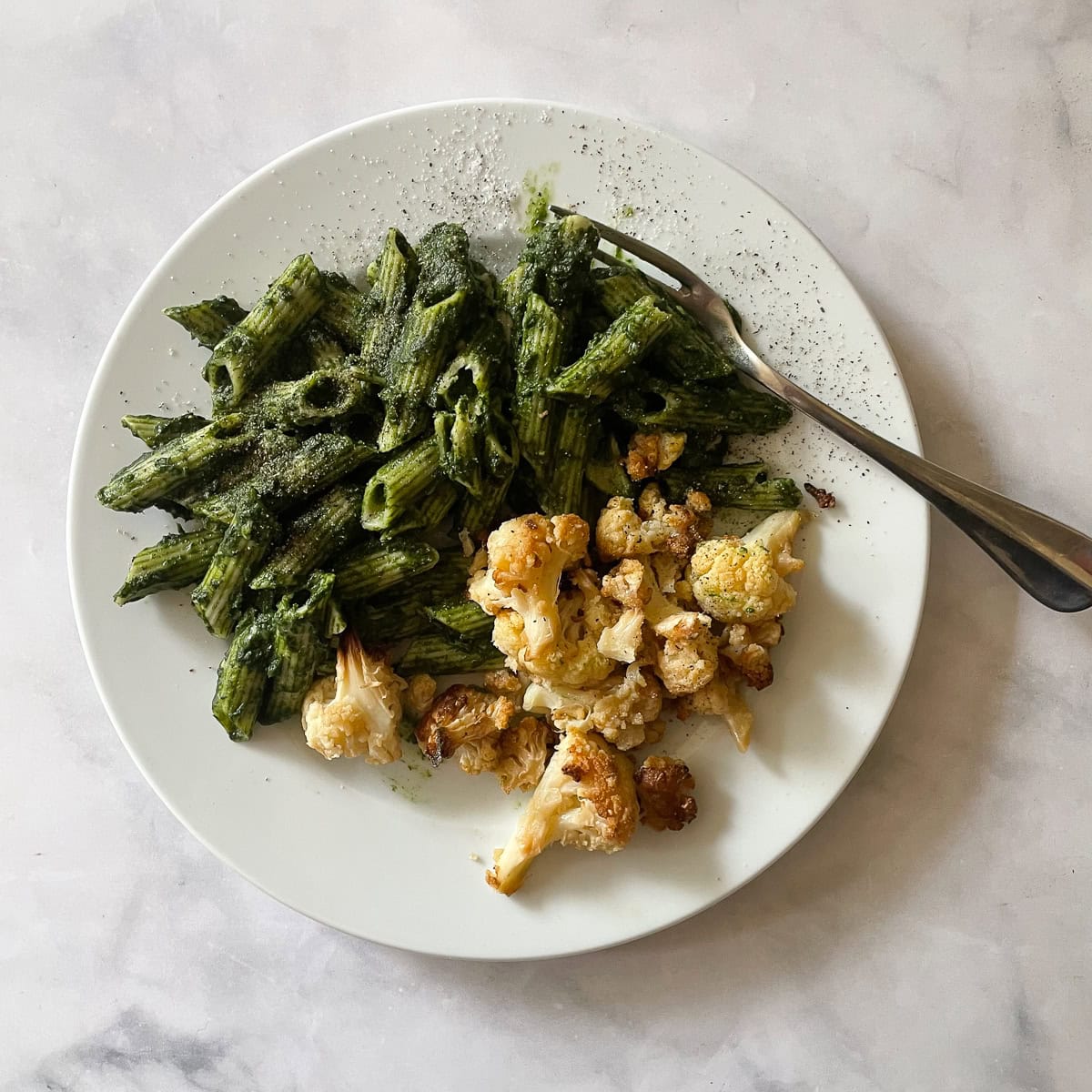 A white plate of kale pasta sauce and roasted cauliflower.