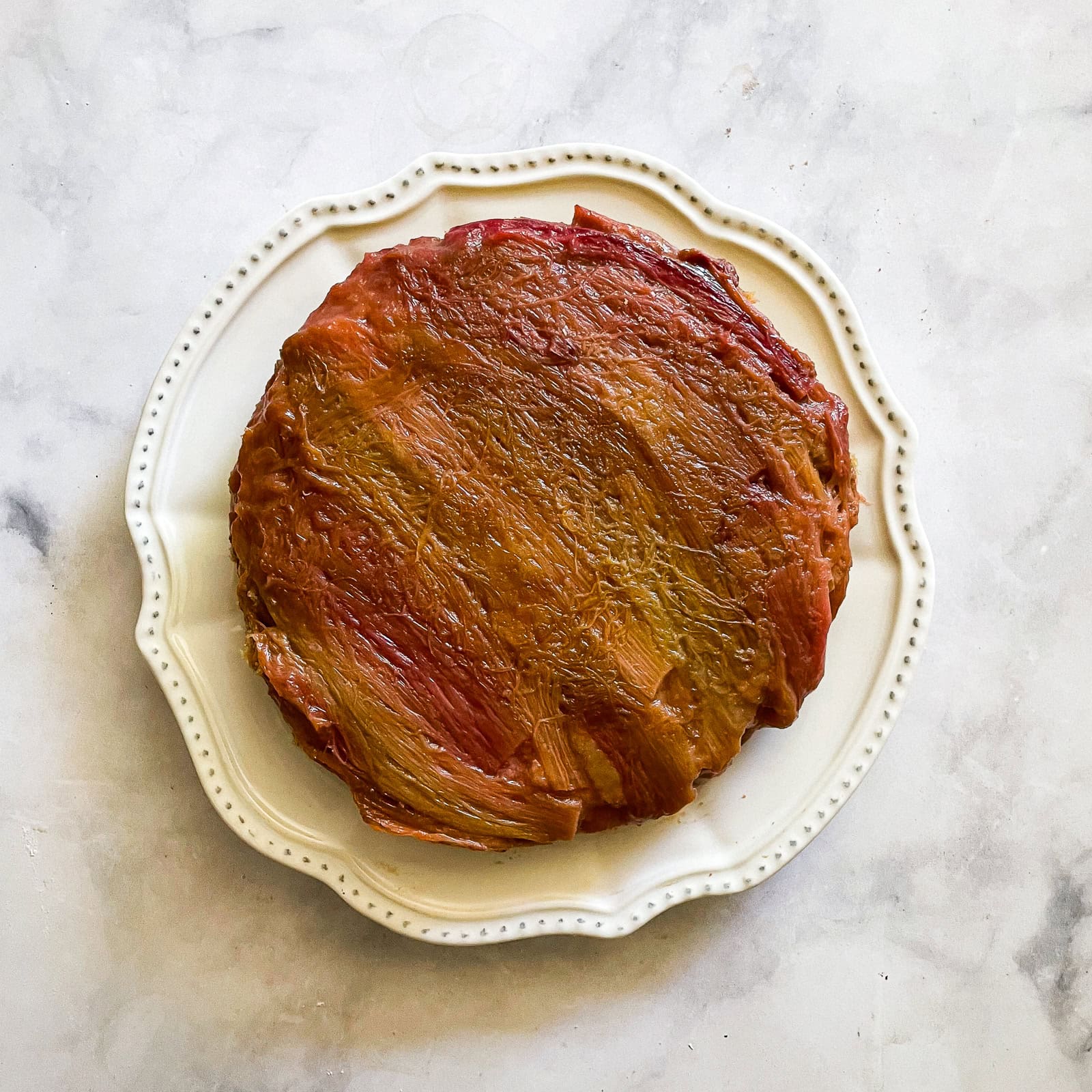 An upside-down rhubarb cake on a white plate.