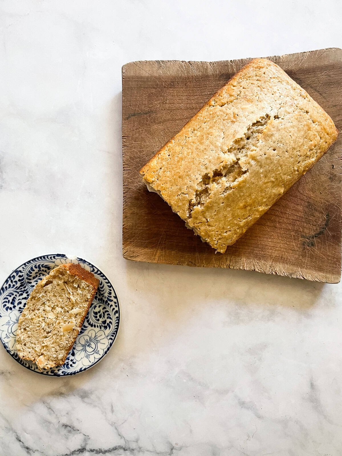 A cinnamon-kissed coconut loaf cake packed with bits of flaked coconut. Inspired by the classic Bill Granger recipe from "Australian Food." A slice of coconut loaf cake on a plate with the loaf next to it.