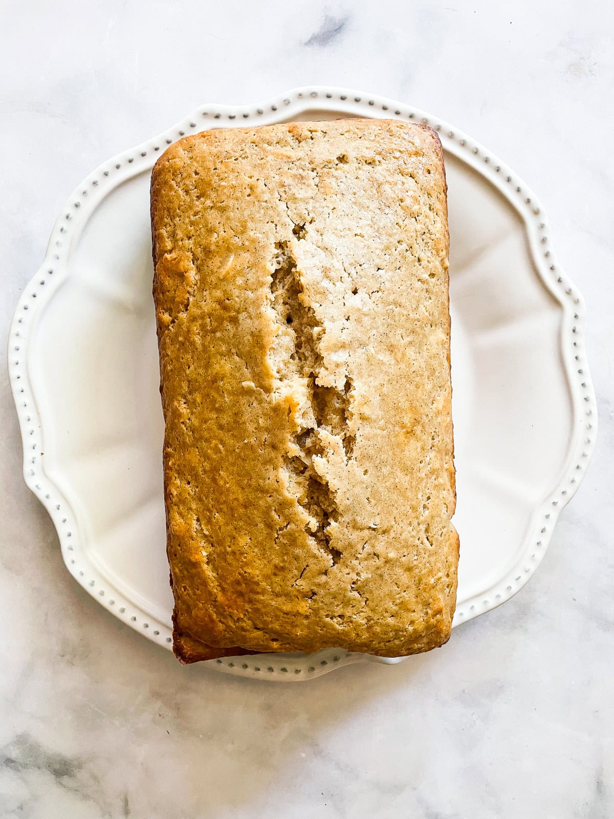 A cinnamon-kissed coconut loaf cake packed with bits of flaked coconut. Inspired by the classic Bill Granger recipe from "Australian Food." A coconut loaf cake on a white plate.