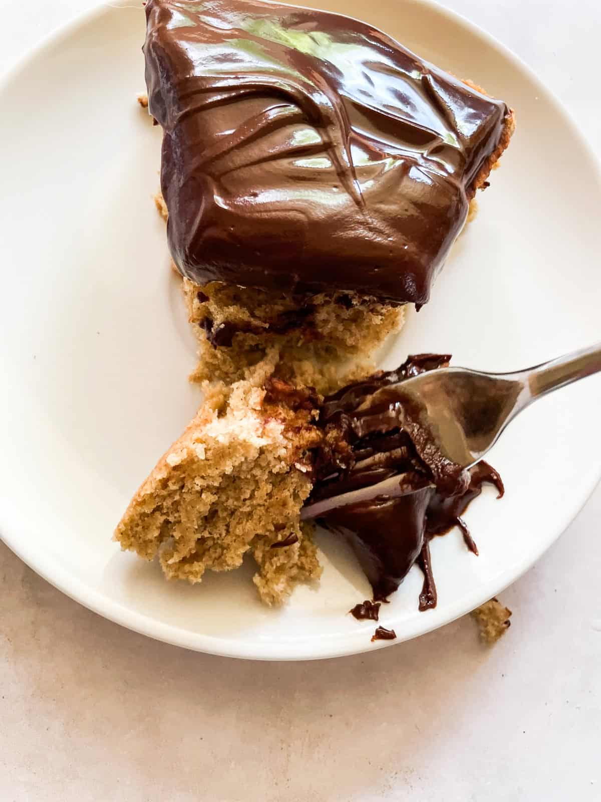 A lusciously moist, spice-kissed banana cake with chocolate frosting is the simplest recipe that always manages to impress! A fork cuts into a slice of banana cake with chocolate frosting.