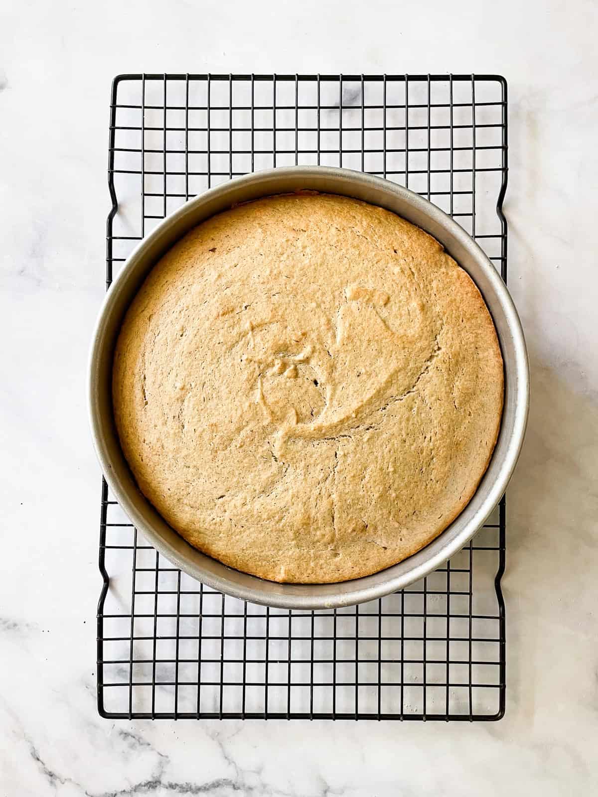 A lusciously moist, spice-kissed banana cake with chocolate frosting is the simplest recipe that always manages to impress! A baked banana cake cools in the cake pan.
