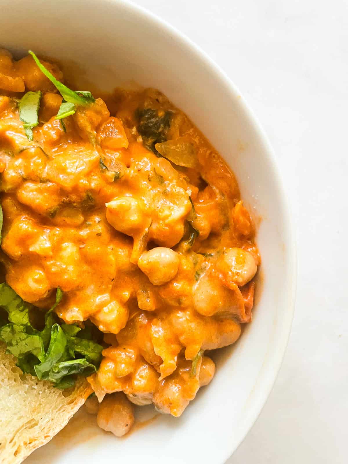 Marry me chickpeas is a vegetarian twist on a popular dish, featuring tender chickpeas and spinach in a tomato broth plus a splash of cream. Marry me chickpeas in a white bowl.