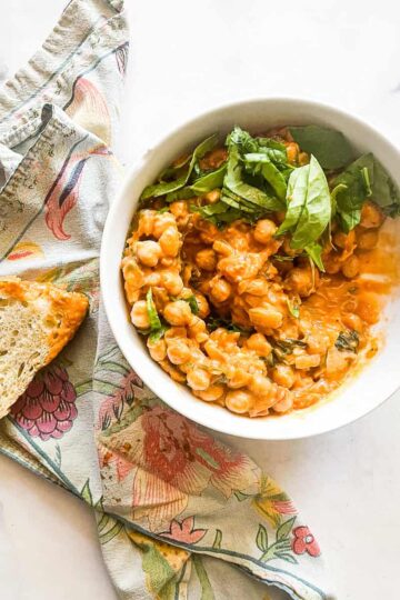 A bowl of marry me chickpeas with bread and a napkin.