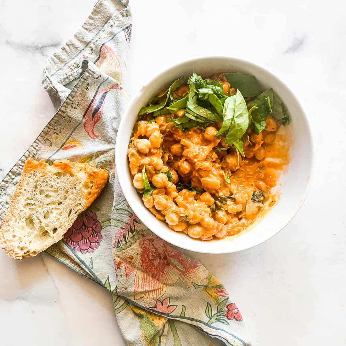 A bowl of marry me chickpeas with bread and a napkin.