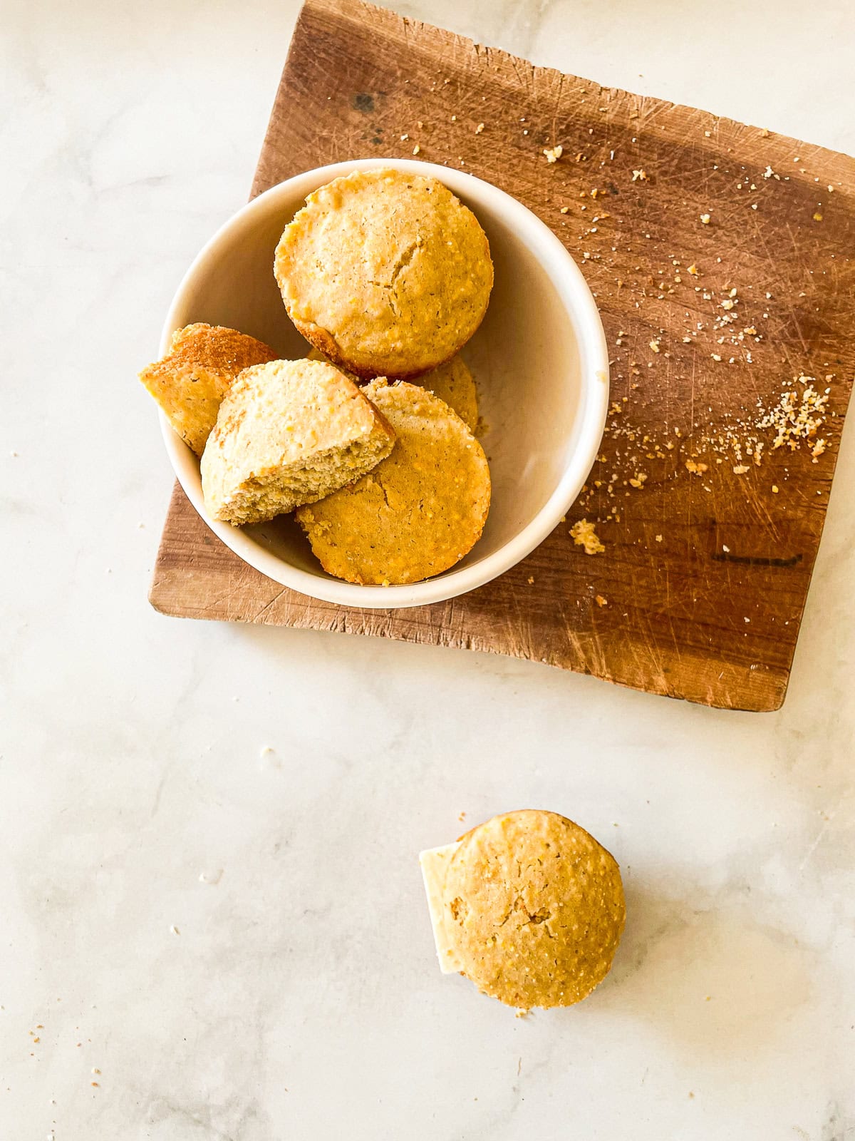 A simple recipe for gluten free cornbread muffins that are as welcome on the Thanksgiving table as they are with a bowl of soup. Gluten free cornbread muffins in a bowl on a cutting board.