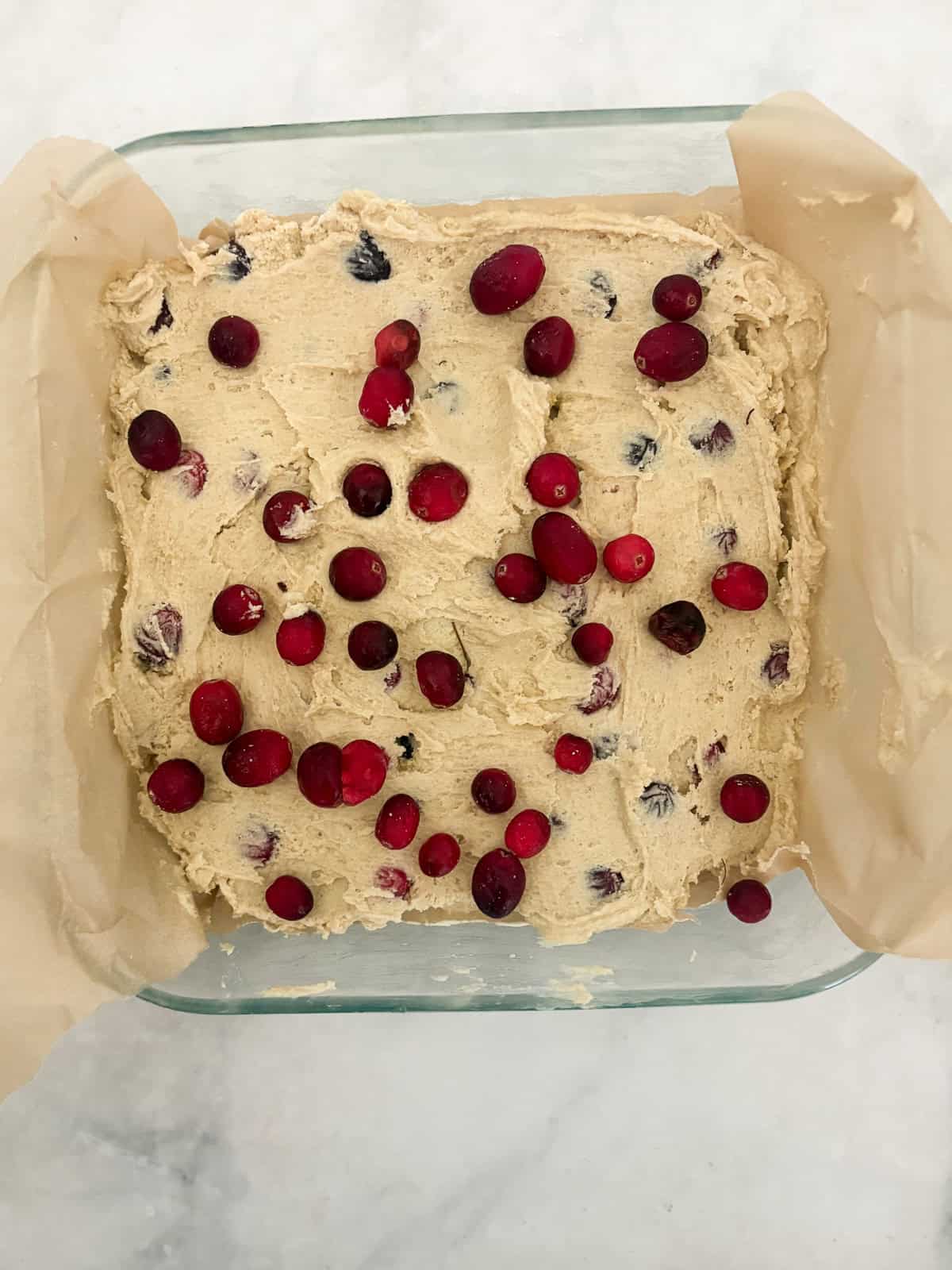 Studded with juicy berries, this sweet and soft cranberry cake is a lovely holiday bake. Great with brunch, or as dessert with ice cream. Cranberry cake batter is added to a lined baking pan.