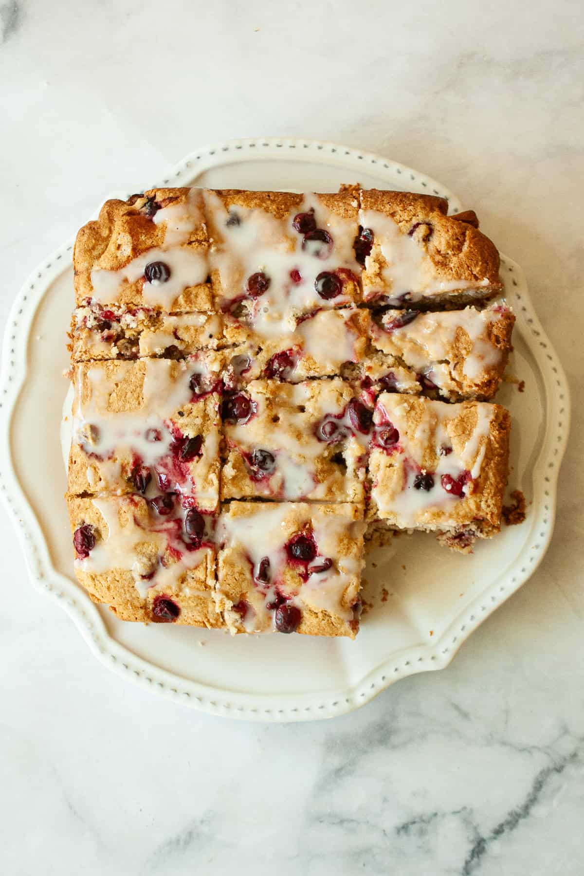 Studded with juicy berries, this sweet and soft cranberry cake is a lovely holiday bake. Great with brunch, or as dessert with ice cream. A sliced cranberry cake on a plate.
