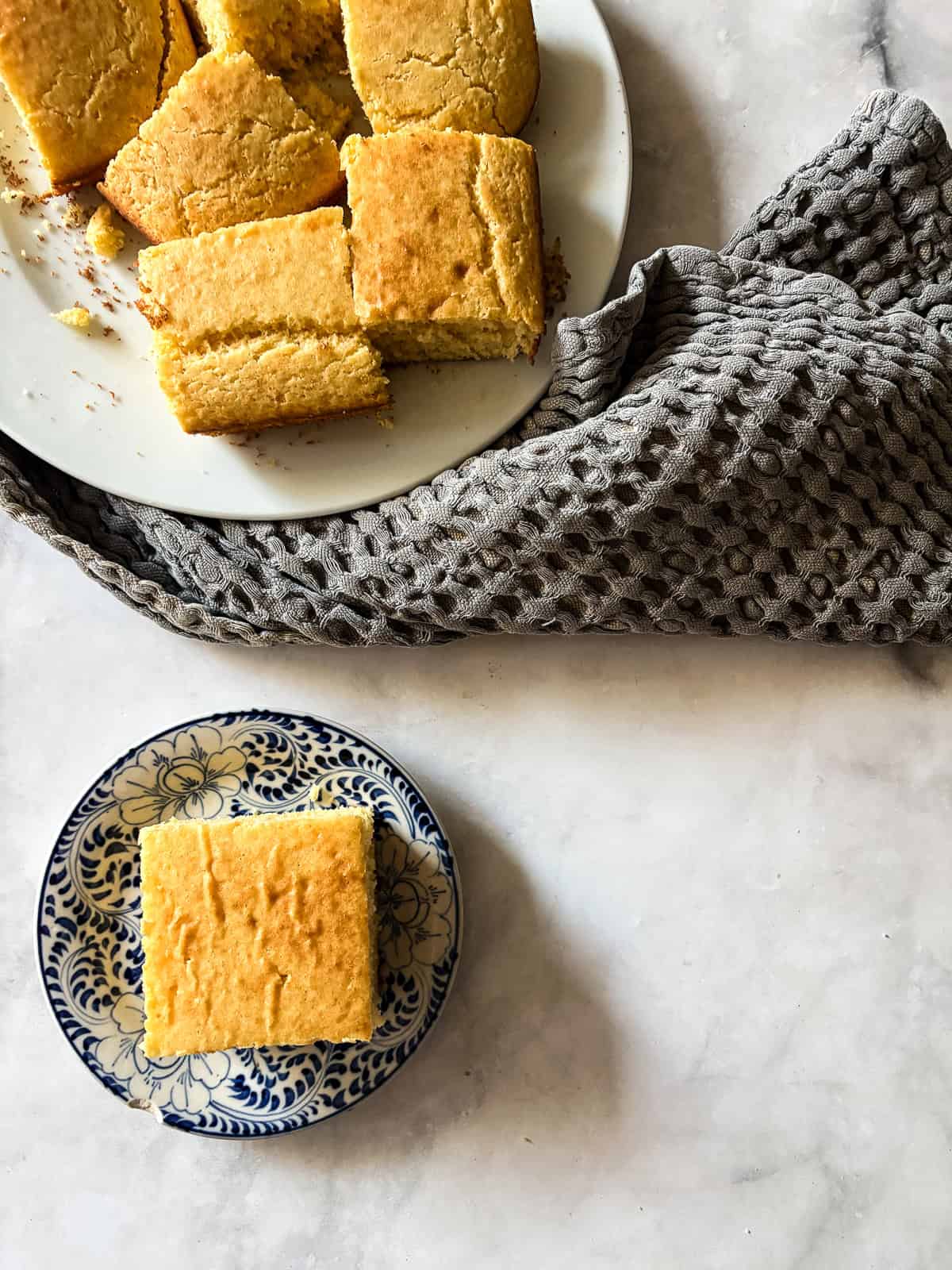 A delicious, lightly sweet homemade cornbread recipe that's made in 1 bowl. Perfect with your favorite soup, stew or chili. A piece of homemade cornbread on a plate next to a plate of cornbread.