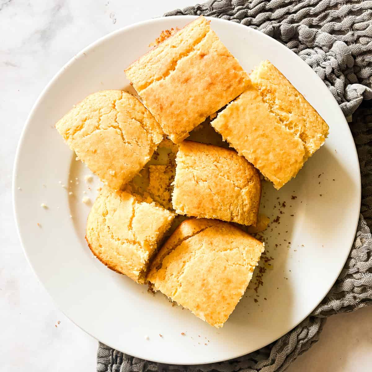 Squares of homemade cornbread on a white serving plate.