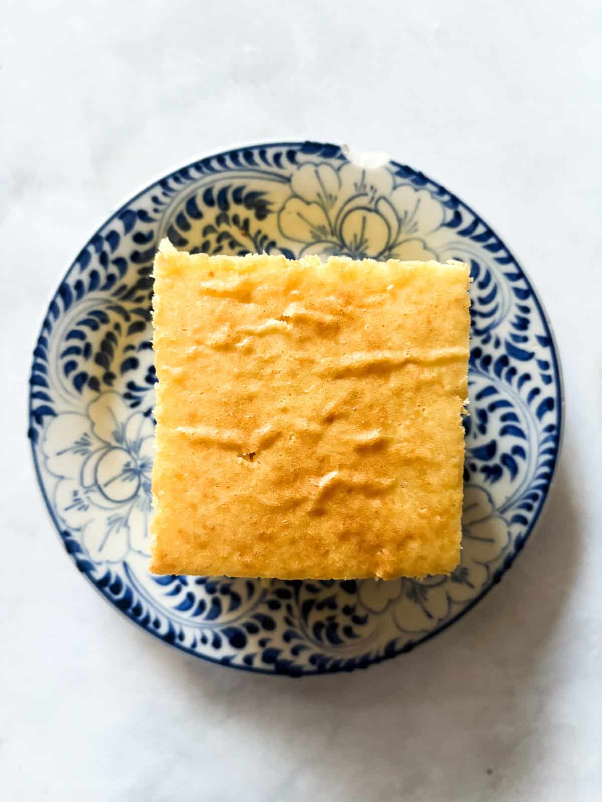 A delicious, lightly sweet homemade cornbread recipe that's made in 1 bowl. Perfect with your favorite soup, stew or chili. A square of homemade cornbread on a blue and white plate.