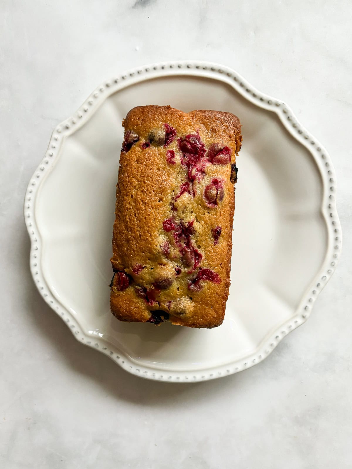 This gorgeous lemon cranberry bread features a lemon-scented loaf swirled with juicy cranberries. Perfect for holiday baking. A loaf of lemon cranberry bread on a plate.