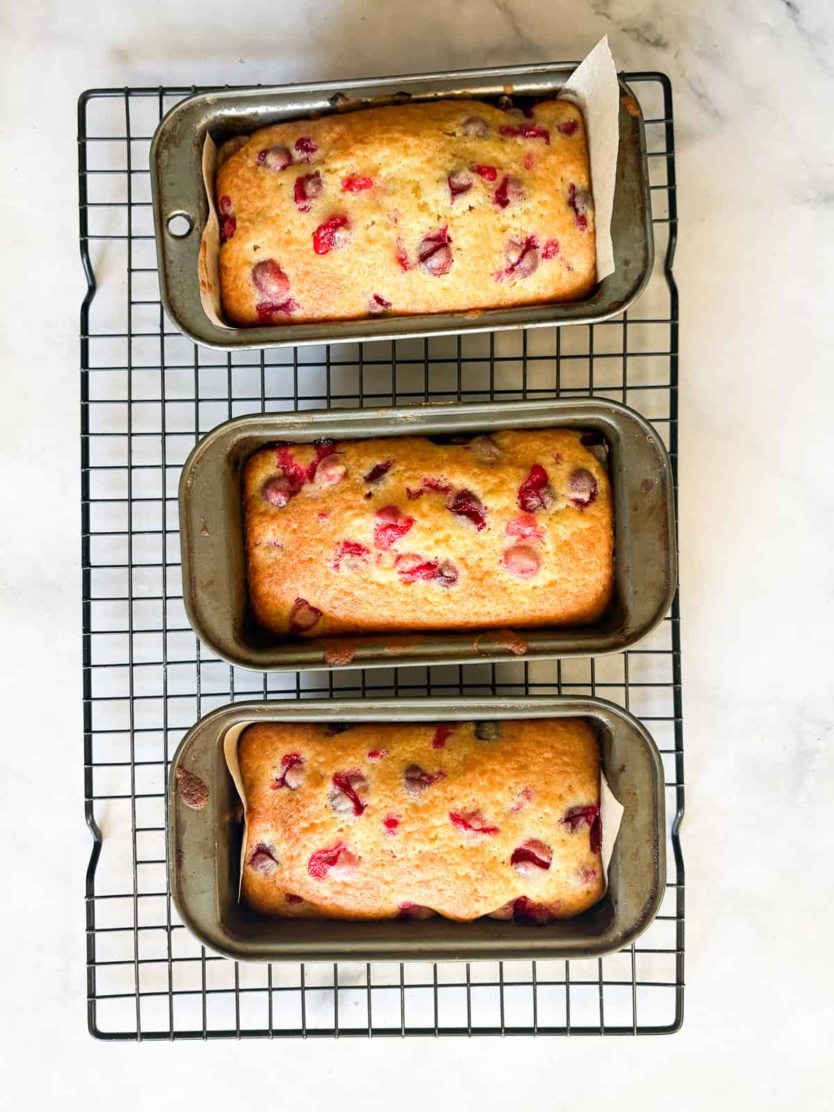 This gorgeous lemon cranberry bread features a lemon-scented loaf swirled with juicy cranberries. Perfect for holiday baking. Three mini loaves of lemon cranberry bread cool on a rack.