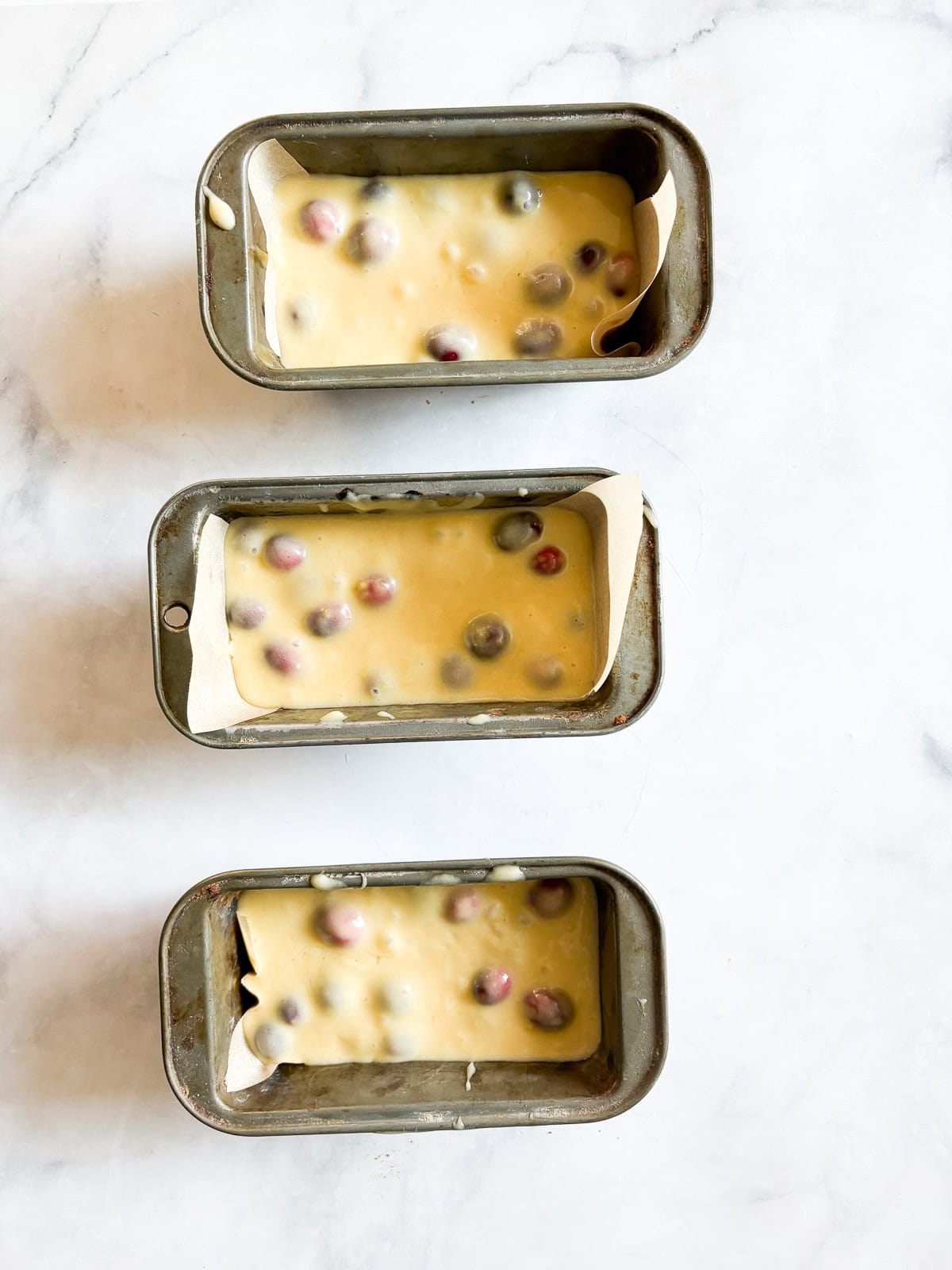 This gorgeous lemon cranberry bread features a lemon-scented loaf swirled with juicy cranberries. Perfect for holiday baking. Three mini loaf pans willed with lemon cranberry bread batter.