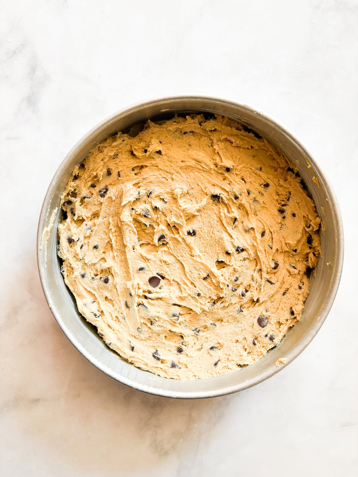 This buttery chocolate chip cookie cake is made with whole wheat flour and brown sugar for a touch of caramel sweetness. Chocolate chip cake batter in a round baking pan.