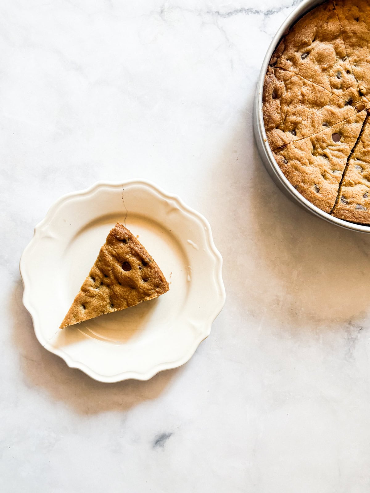 This buttery chocolate chip cookie cake is made with whole wheat flour and brown sugar for a touch of caramel sweetness. A slice of chocolate chip cookie cake on a plate with the sliced cake to the right of it.