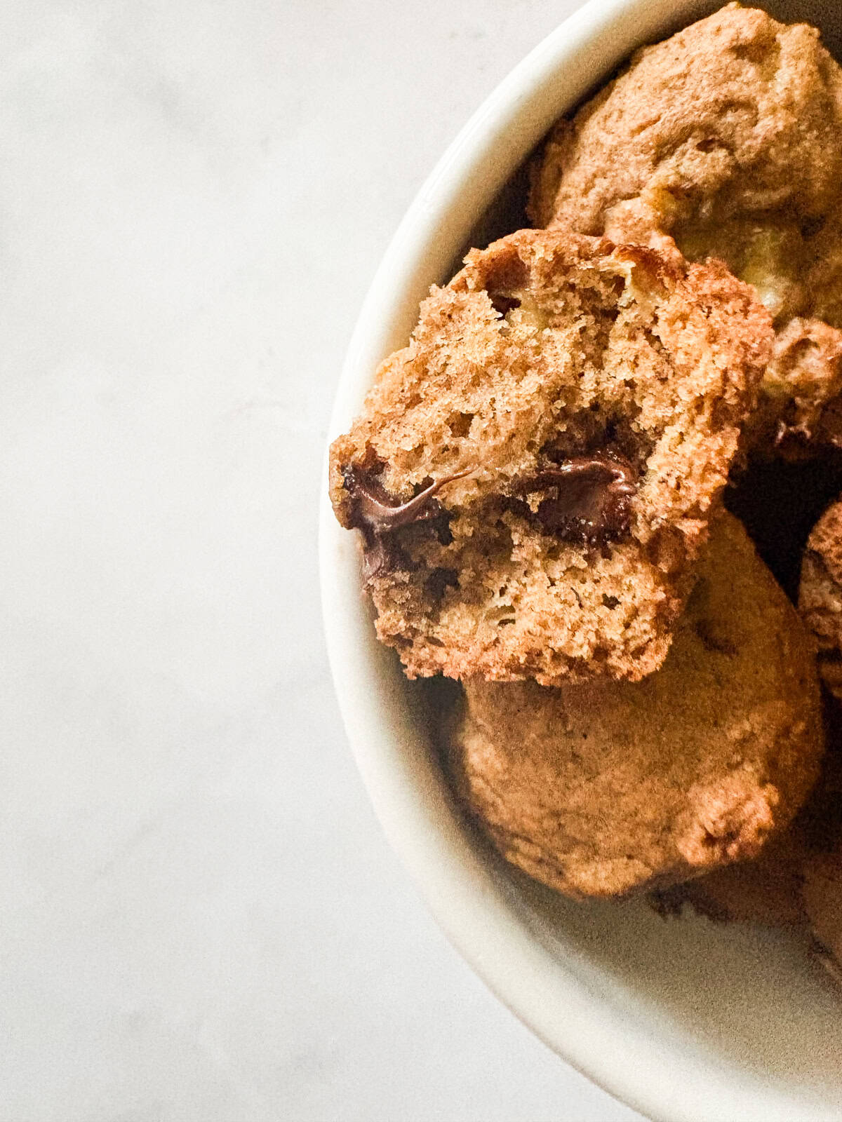 These perfect bite-sized mini banana muffins are made with whole-grain flour, maple syrup, and heart-healthy olive oil. Chocolate chips peek our of a mini banana muffin.