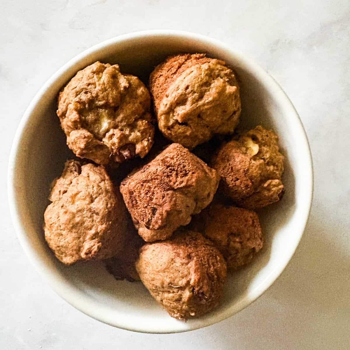 A bunch of mini banana muffins in a white bowl.