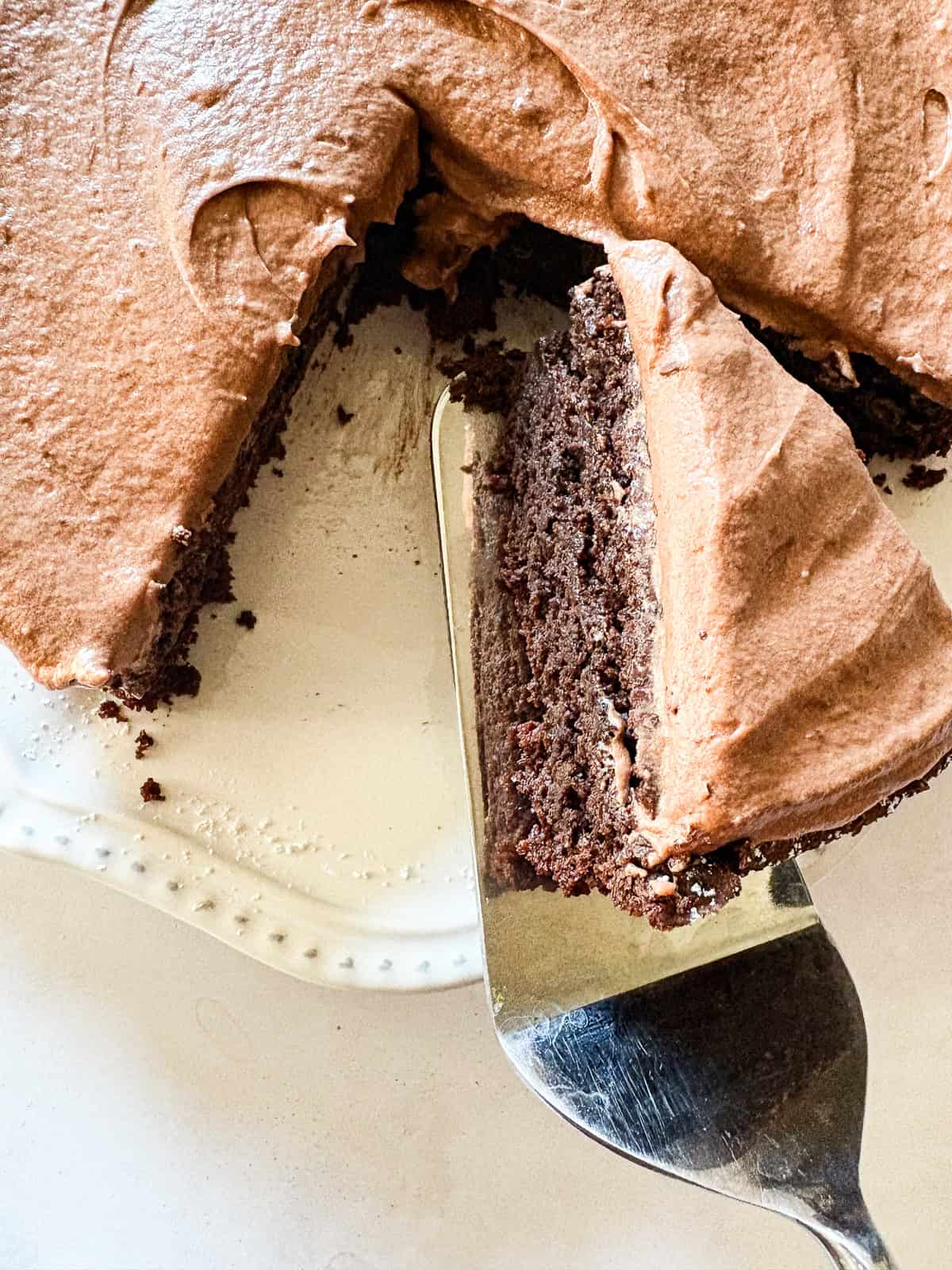 A beyond easy one-layer vegan chocolate cake recipe made in one bowl with pantry staples. Top with your fav frosting. A server lifts a piece of vegan chocolate cake out of the cake.