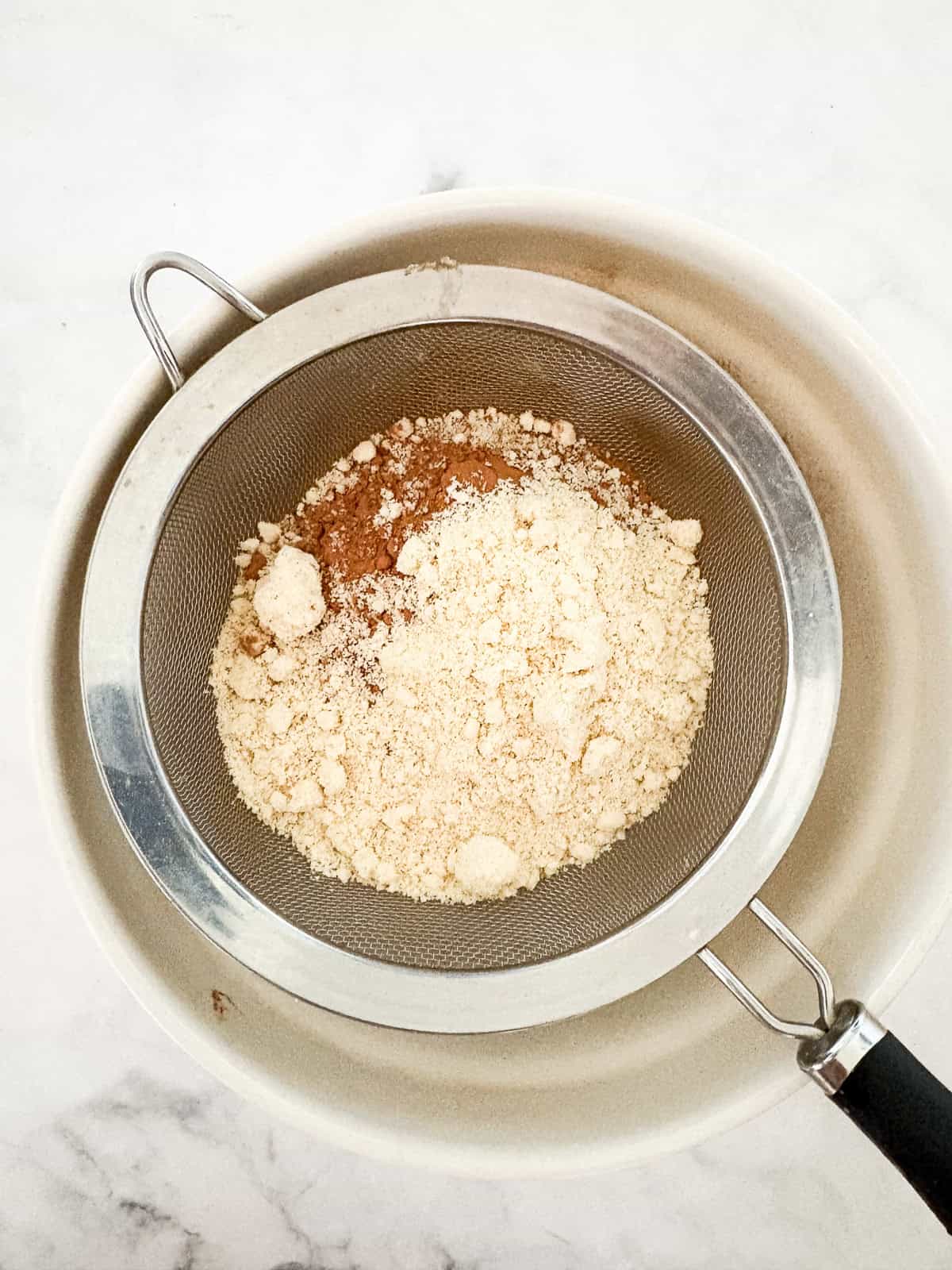 A beyond easy one-layer vegan chocolate cake recipe made in one bowl with pantry staples. Top with your fav frosting. Dry ingredients for vegan chocolate cake sifted into a bowl.