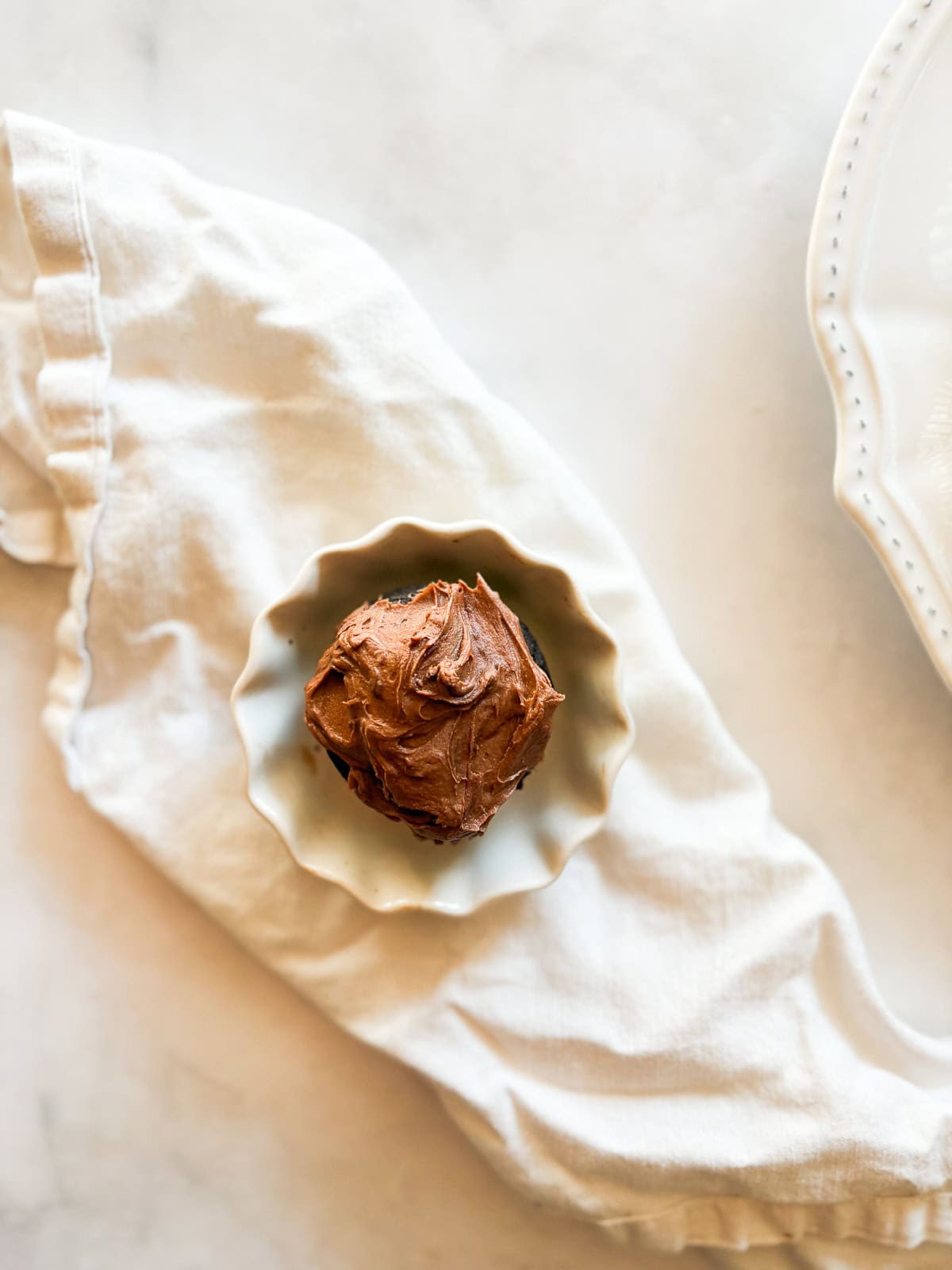 Tender, chocolatey vegan chocolate cupcakes frosted with a sumptuous vegan chocolate buttercream are out-of-this-world good! A vegan chocolate cupcake in a decorative plate on a napkin.