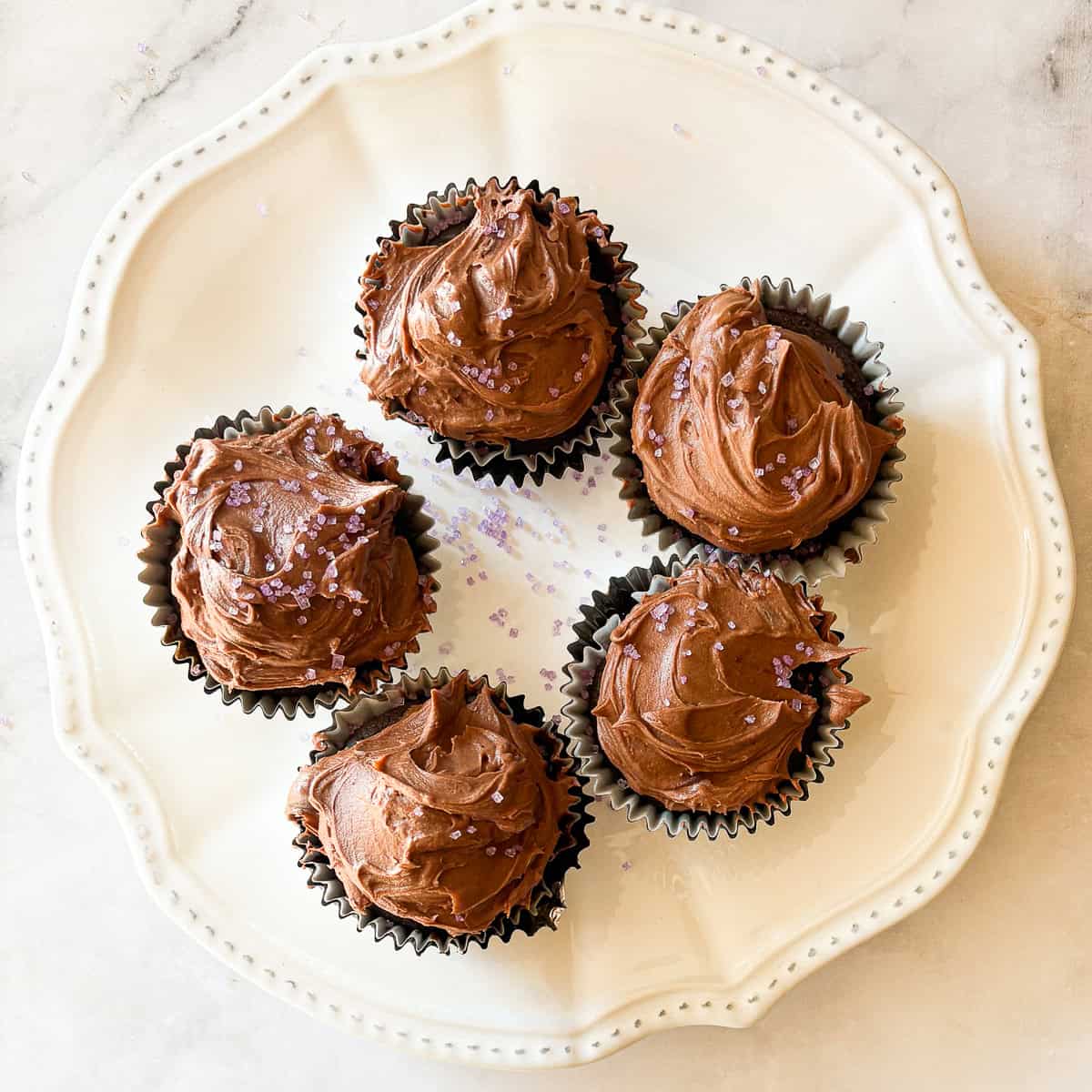 Four vegan chocolate cupcakes on a plate.